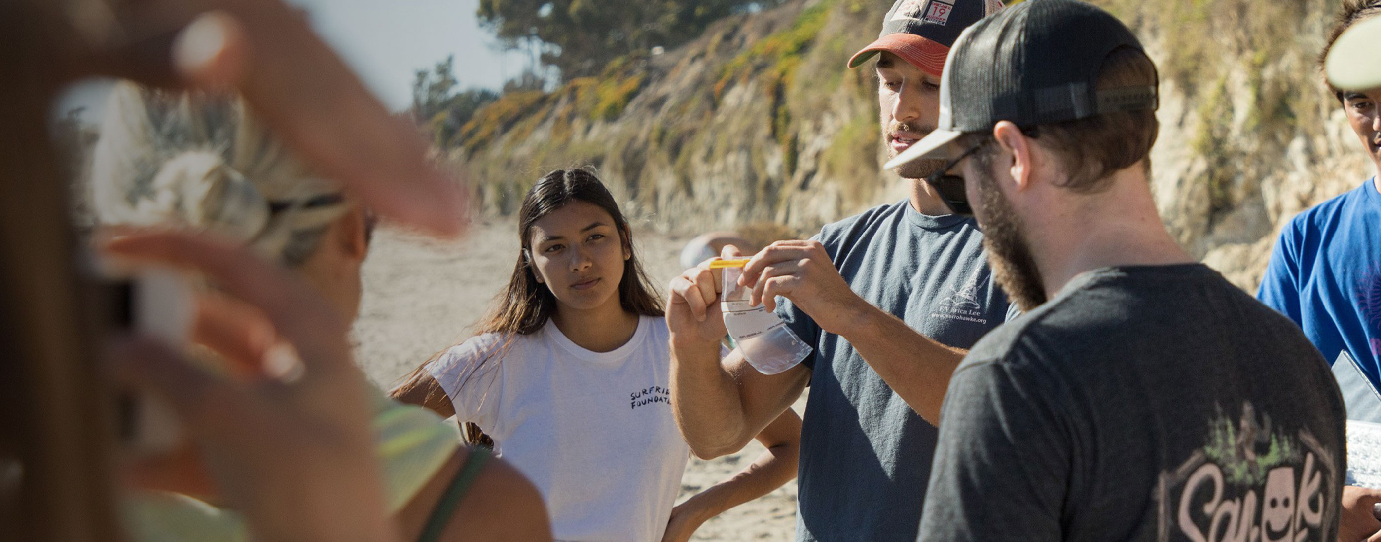 A group of volunteers are gathered in an outdoor space looking at a water sample